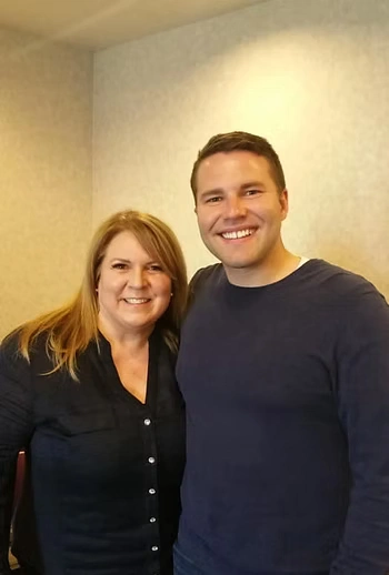 A photo of two adult siblings, one younger, one older. They are both smiling brightly