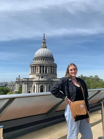 A woman poses on a terrace with St. Paul’s Cathedral in the background under a clear blue sky.