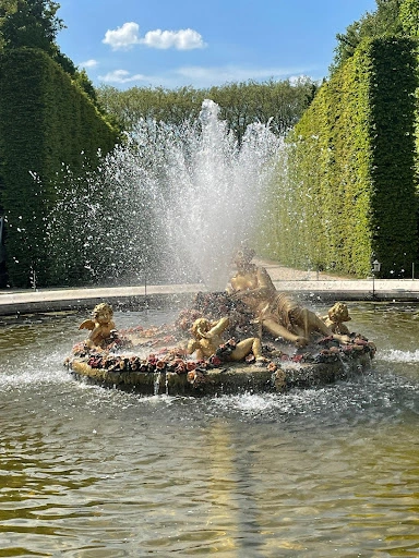Versailles fountain with gilded statues and water spraying upward.