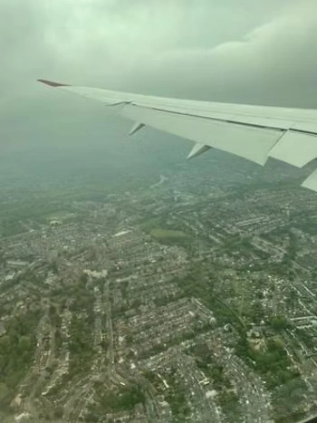 An airplane wing over a sprawling city seen through hazy clouds