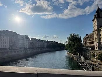 A calm river lined with historic buildings under a bright sky with soft clouds.