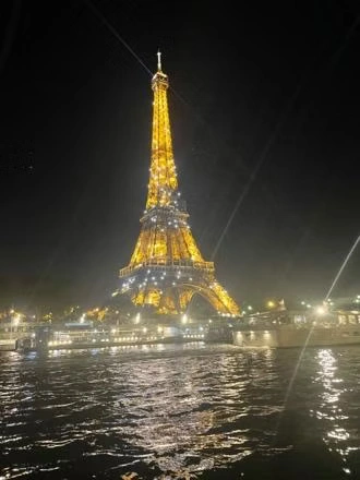 The Eiffel Tower glowing gold against the night time sky with reflections shimmering on the river below.